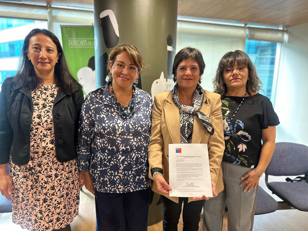 Junto a la seremi y a profesionales de ambos servicios, la Defensora Nacional muestra la carta que formaliza el ingreso de la instituci&oacute;n al programa.